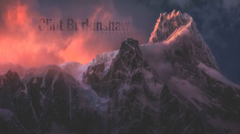 Snow-capped mountain peaks lit red by the sunrise, with Clint Burkinshaw Photography written across the sky